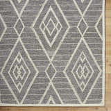 Close-up of the Ceanna Area Rug; gray wool with off-white geometric diamond pattern and textured hand-tufted construction. Corner