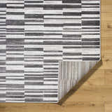 Close-up of the Cemach Cream Area Rug showing its charcoal, gray, and silver horizontal block pattern and woven texture. Fold