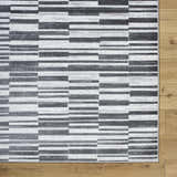 Close-up of the Cemach Cream Area Rug featuring a contemporary gray and white geometric pattern on wood floors. Corner