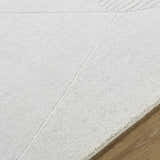 Close-up of the ivory Carpus Area Rug showing its subtle geometric pattern and soft wool texture on a wood floor. Texture