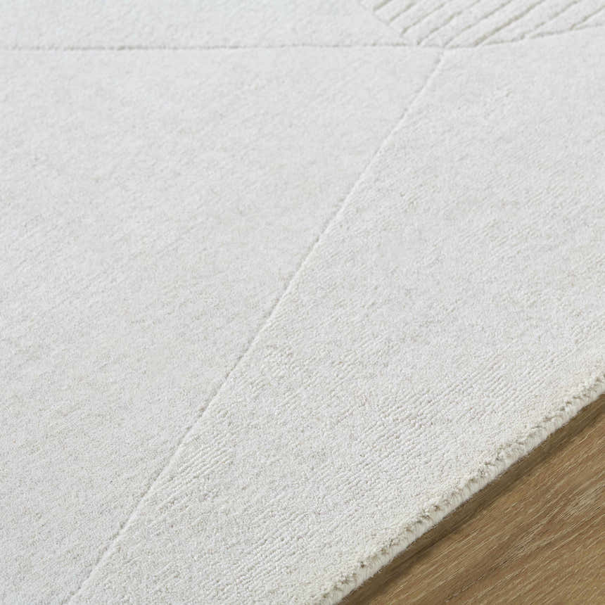 Close-up of the ivory Carpus Area Rug showing its subtle geometric pattern and soft wool texture on a wood floor. Texture