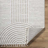 Close-up of the Cassie Area Rug showing cream and peach stripes and semicircle design with tassels on a wood floor. Fold