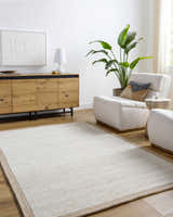 Living room scene with a beige and ivory Cianna Area Rug, wood cabinet, and white armchairs. Roomscene-Rectangle