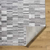 Close-up of Cherie Medium Gray Area Rug showing a contemporary geometric pattern and polypropylene material on wood floor. Fold