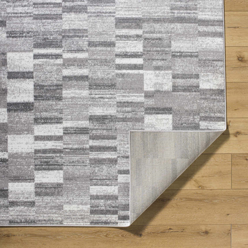 Close-up of Cherie Medium Gray Area Rug showing a contemporary geometric pattern and polypropylene material on wood floor. Fold