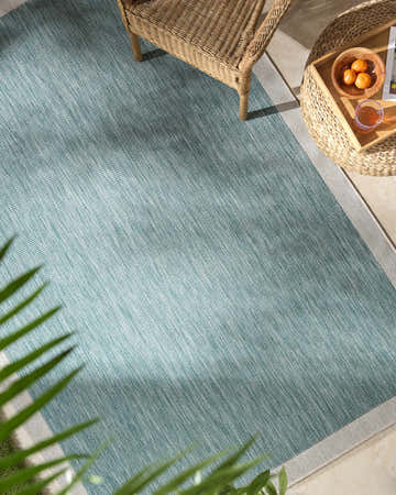 Outdoor patio scene with Chetan Light Blue rug, wicker chair and table. Roomscene-Rectangle