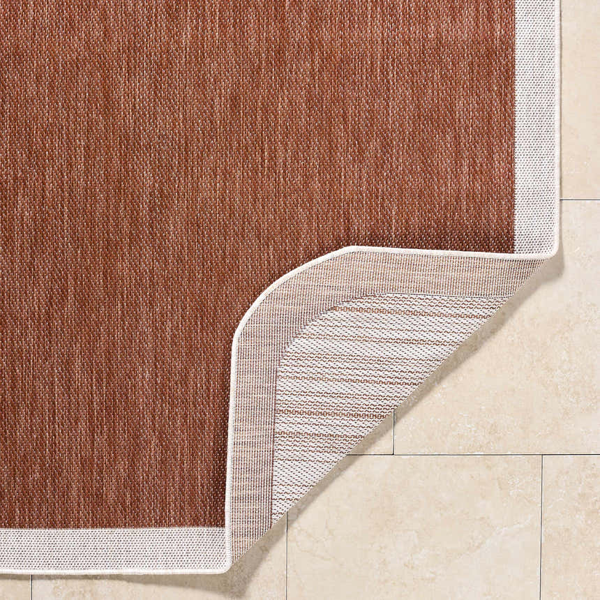 Close-up of the Chetan Brown Outdoor Rug showing its woven texture, cream border, and polypropylene backing. Fold