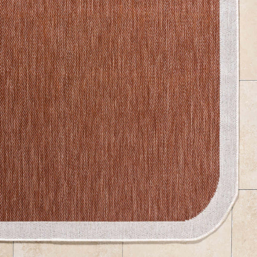Close-up of the Chetan Brown Outdoor Rug. The rug has a woven texture and a cream border. Corner