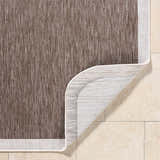 Close-up of the Chetan Dark Brown Area Rug showing texture, cream border, and non-slip backing on beige tile. Fold