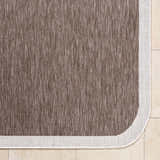 Close-up of the Chetan Dark Brown Area Rug showing its woven texture and cream border on beige tile. Corner