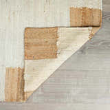 Close up of the hand woven Rocio White Jute Carpet showing its cream and tan color block design and textured jute fibers. Fold