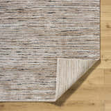 Close-up of Wantu Luxe Thick Area Rug showing ivory, tan, and black horizontal stripes and folded corner on wood floor. Fold