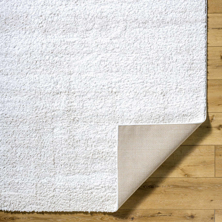 Close-up of the Arlind Area Rug showing its white shag texture and woven backing on a wood floor. Fold