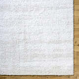Close-up of the Arlind Area Rug showing its white shag texture on a light wood floor. Corner