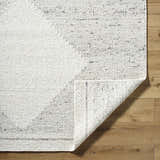 Close-up of the Ethara Ivory Charcoal rug showing the wool texture and global pattern on a wood floor. Fold