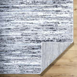 Close-up of the Azmina Area Rug featuring a contemporary striped pattern in black, ivory, light blue, and gray. Fold