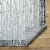 Close-up of Dhaval Black Area Rug showing charcoal, light gray colors, and machine woven texture on wood floor. Fold