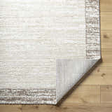 Close-up of the Dhaval Ivory Area Rug showing its cream color, light brown border, and machine-woven texture. Fold