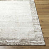 Close-up of the Dhaval Ivory Area Rug showing its cream color, light brown border, and soft texture on a wood floor. Front
