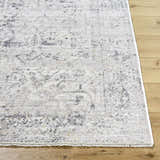Close-up of Alivia Area Rug showing its charcoal, gray, and ivory traditional pattern and fringe on light wood floor. Front