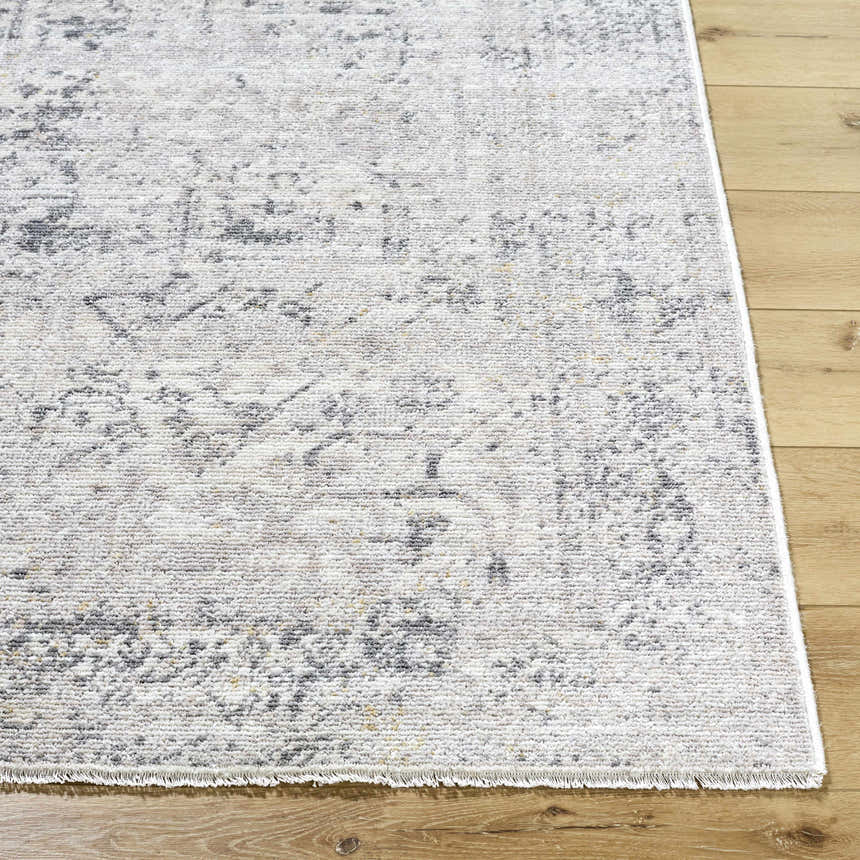 Close-up of Alivia Area Rug showing its charcoal, gray, and ivory traditional pattern and fringe on light wood floor. Front