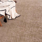 Close-up of the light brown Leanna Washable Area Rug with a subtle geometric pattern and a throw blanket. Styleshot