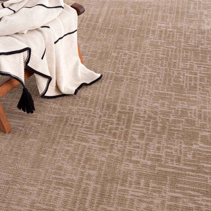 Close-up of the light brown Leanna Washable Area Rug with a subtle geometric pattern and a throw blanket. Styleshot