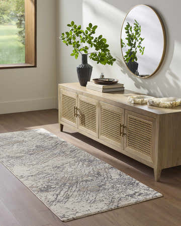 Entryway scene with a cream and charcoal Aolani rug, wood floors, and a light wood console table with a round mirror. Roomscene-Runner