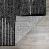 Close-up of the Stephan Area Rug showing its black, charcoal, and cream contemporary pattern and durable polypropylene material. Fold