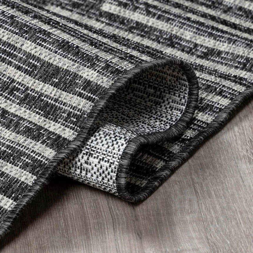 Close-up of the Stephan Area Rug showing its black, charcoal, and cream striped pattern and woven texture. Fold