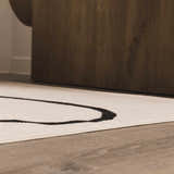 Close up of the Eilir Boho Rug in bone and onyx black with a geometric pattern under a wood table. Styleshot