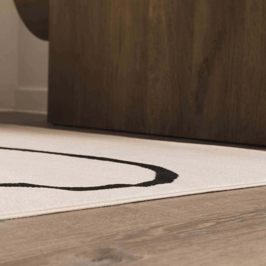Close up of the Eilir Boho Rug in bone and onyx black with a geometric pattern under a wood table. Styleshot