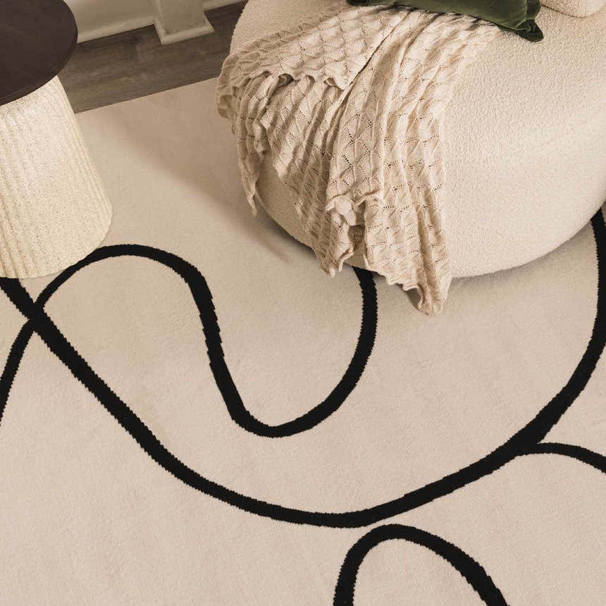 Close-up of the Eilir Modern Boho Rug featuring a bone color and bold, black abstract line design, styled with a round chair. Styleshot