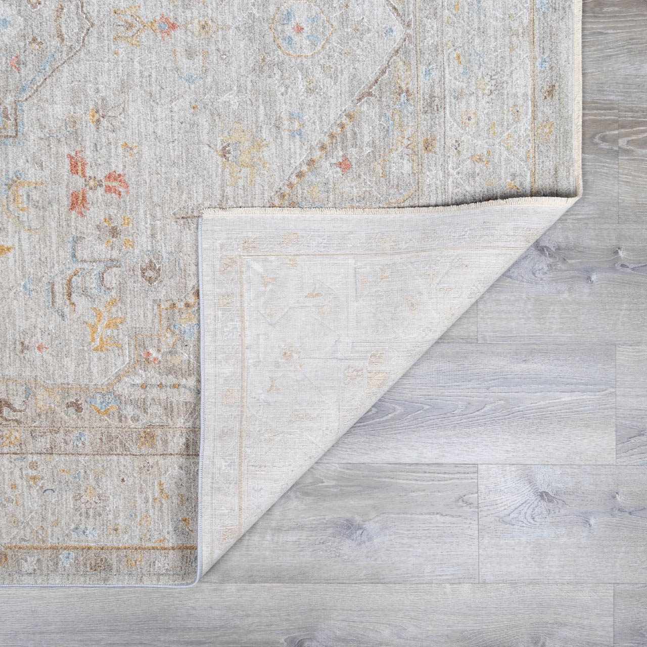 Close-up of the Engin Thick Luxe Area Rug showing its traditional amber, pink, and gray pattern and woven texture. Fold