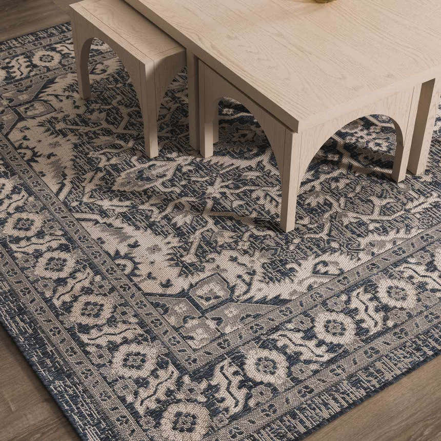Close-up of the Etoile Navy Blue Performance Rug with a traditional floral pattern and neutral border under a light wood table. Roomscene-Rectangle