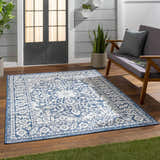 Outdoor patio scene with a blue and white Etoile Navy Blue Performance Rug, gray loveseat, and wood flooring. Roomscene-Rectangle