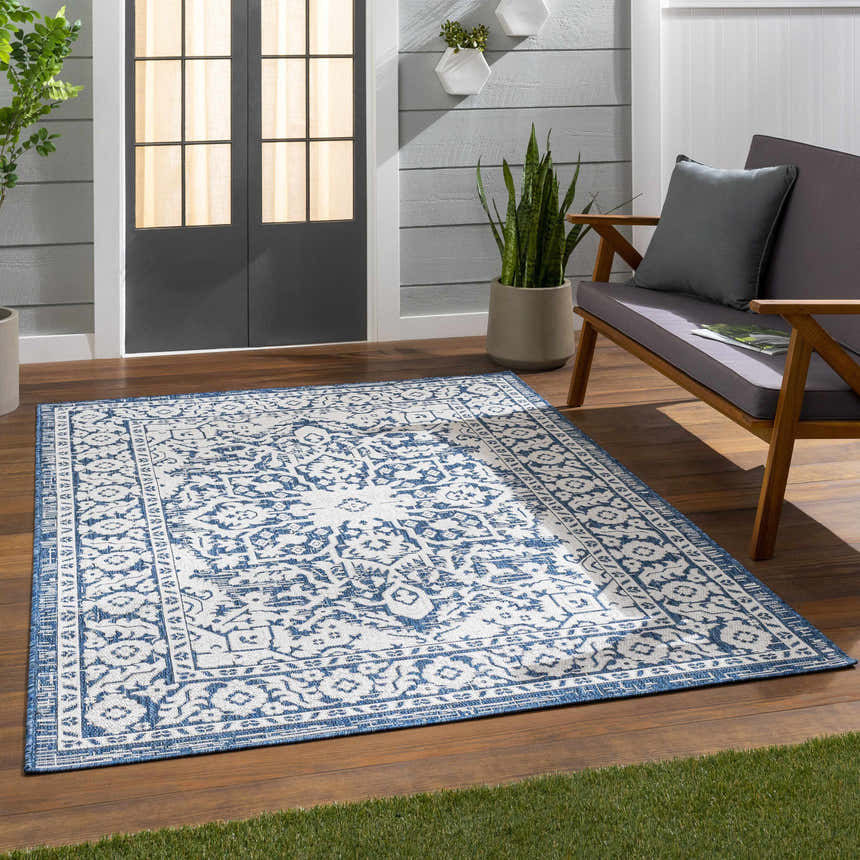 Outdoor patio scene with a blue and white Etoile Navy Blue Performance Rug, gray loveseat, and wood flooring. Roomscene-Rectangle