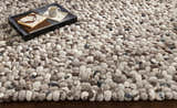 Close-up of the hand woven Fillmore Area Carpet. Wool rug with black, charcoal, cream, and gray pebble design. Styleshot