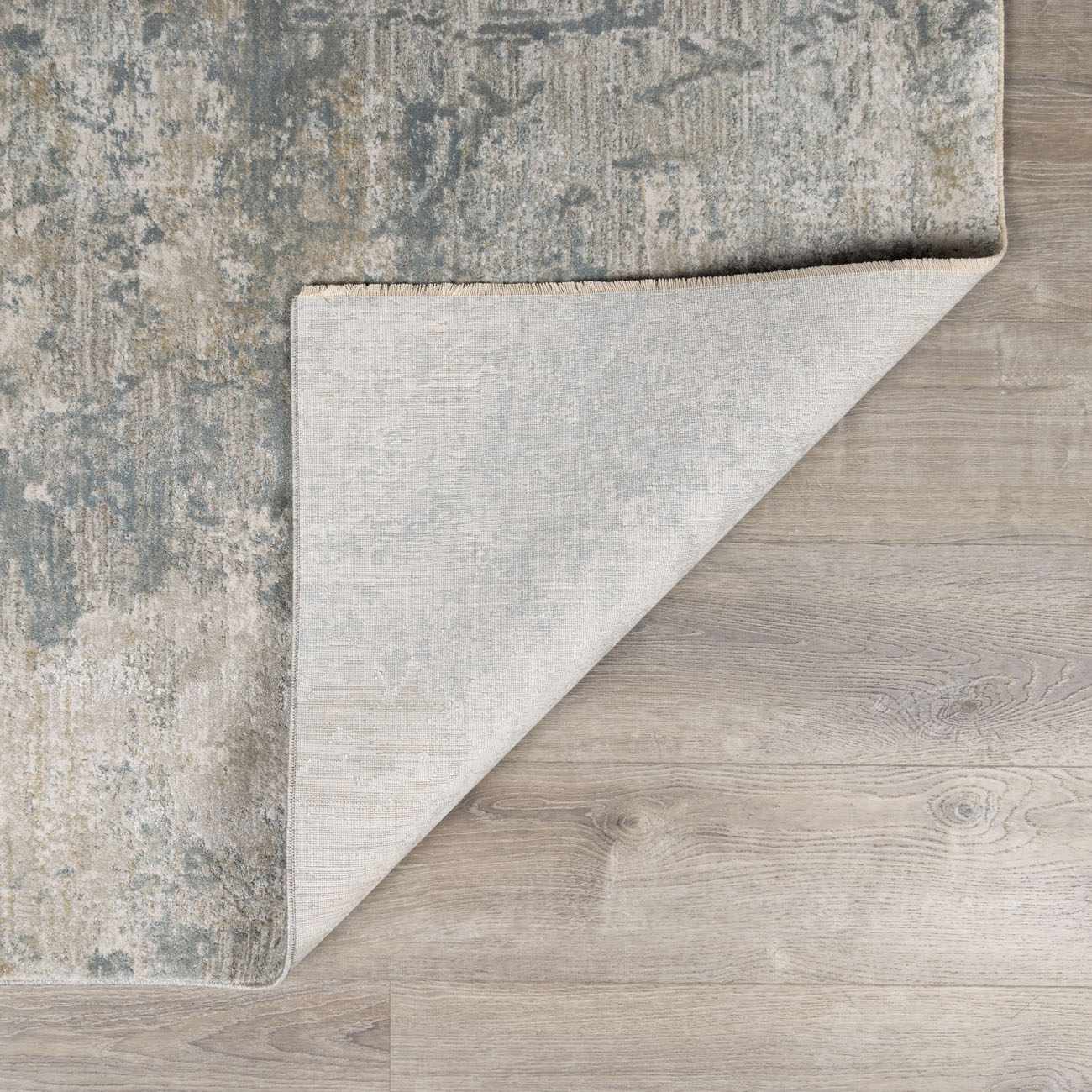 Close-up of the Fallin Gray Thick Luxe Abstract Striped Rug showing its abstract pattern and backing on a wood floor. Fold
