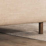 Close-up of the abstract striped Fallin Gray Thick Luxe Rug peeking out from under a beige sofa with dark wood legs. Styleshot