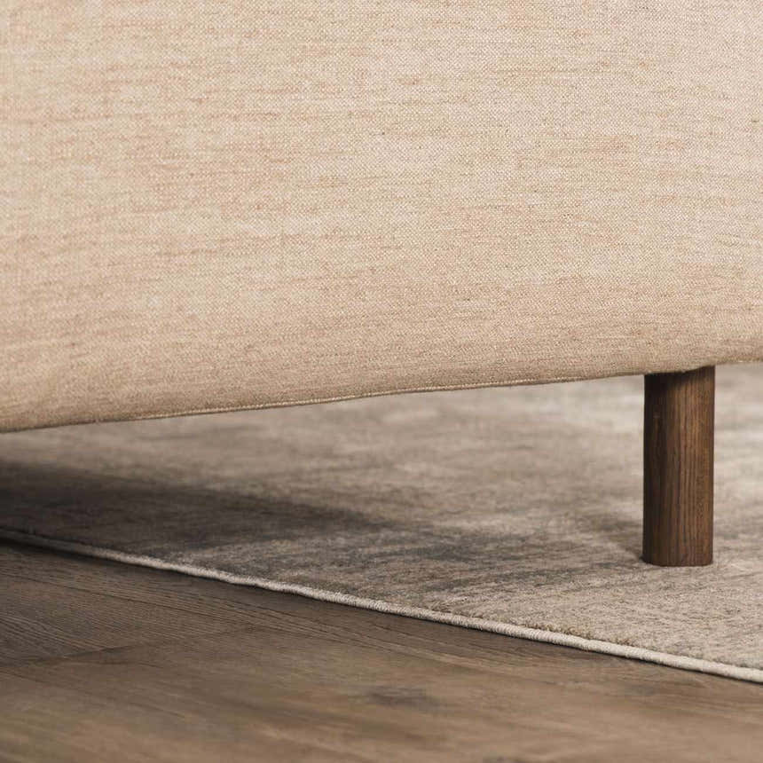 Close-up of the abstract striped Fallin Gray Thick Luxe Rug peeking out from under a beige sofa with dark wood legs. Styleshot