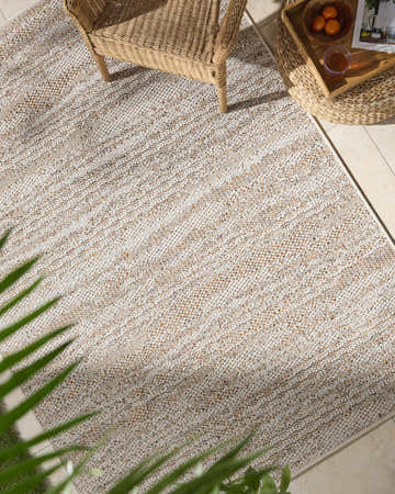 Outdoor patio scene with a beige Alezae Area Rug, wicker chair, and side table. Roomscene-Rectangle