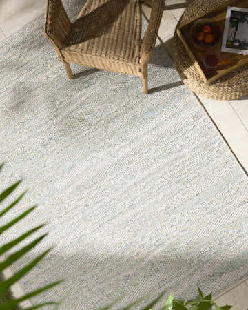 Outdoor patio scene with a wicker chair and Alezae Ivory Area Rug in ivory, light gray, and pale blue. Roomscene-Rectangle