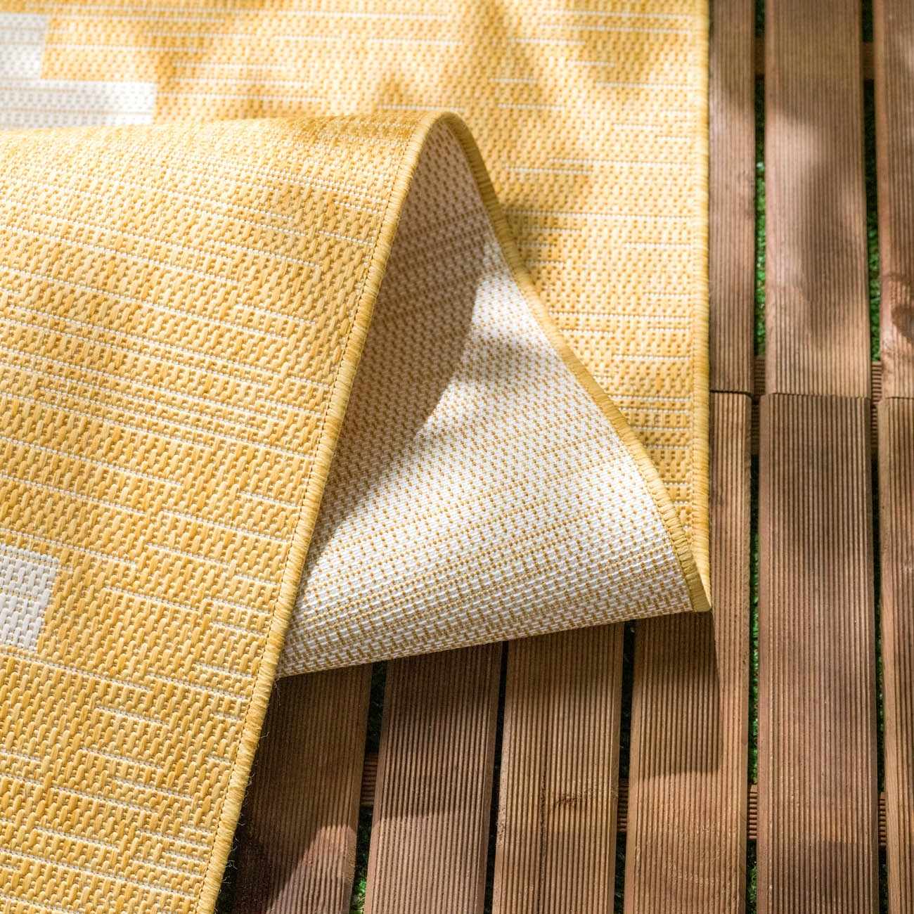 Close-up of the Djugun Yellow Outdoor Rug showing geometric weave, colors, and durable polypropylene material. Fold