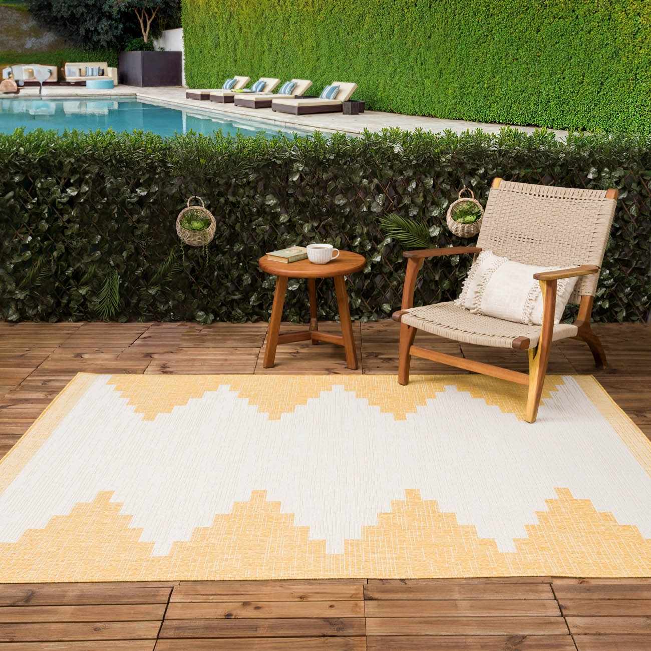 Outdoor patio scene with a Djugun Yellow rug, wooden chair, and table by a pool. Roomscene-Rectangle