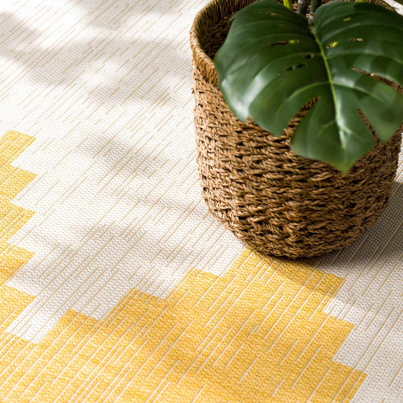 Close-up of the Djugun Yellow Outdoor Rug with a geometric pattern and woven texture next to a plant in a basket. Styleshot