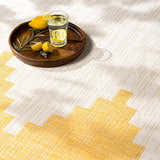 Close-up of the Djugun Yellow Outdoor Rug with geometric pattern and a wood tray holding lemons and a glass of water. Styleshot