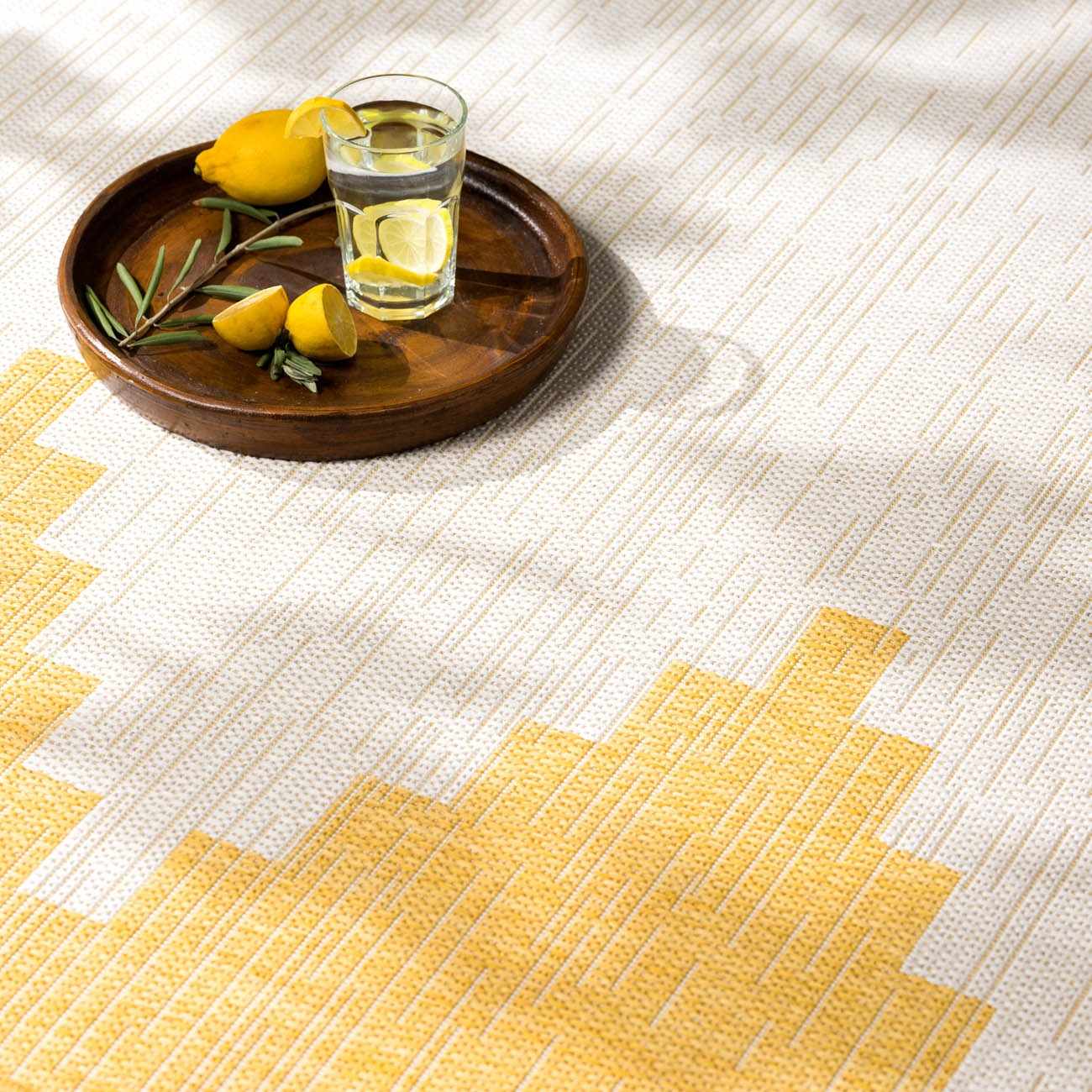 Close-up of the Djugun Yellow Outdoor Rug with geometric pattern and a wood tray holding lemons and a glass of water. Styleshot