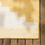 Close-up of the Djugun Yellow Outdoor Rug showing geometric pattern and woven texture on a wood deck. Swatch
