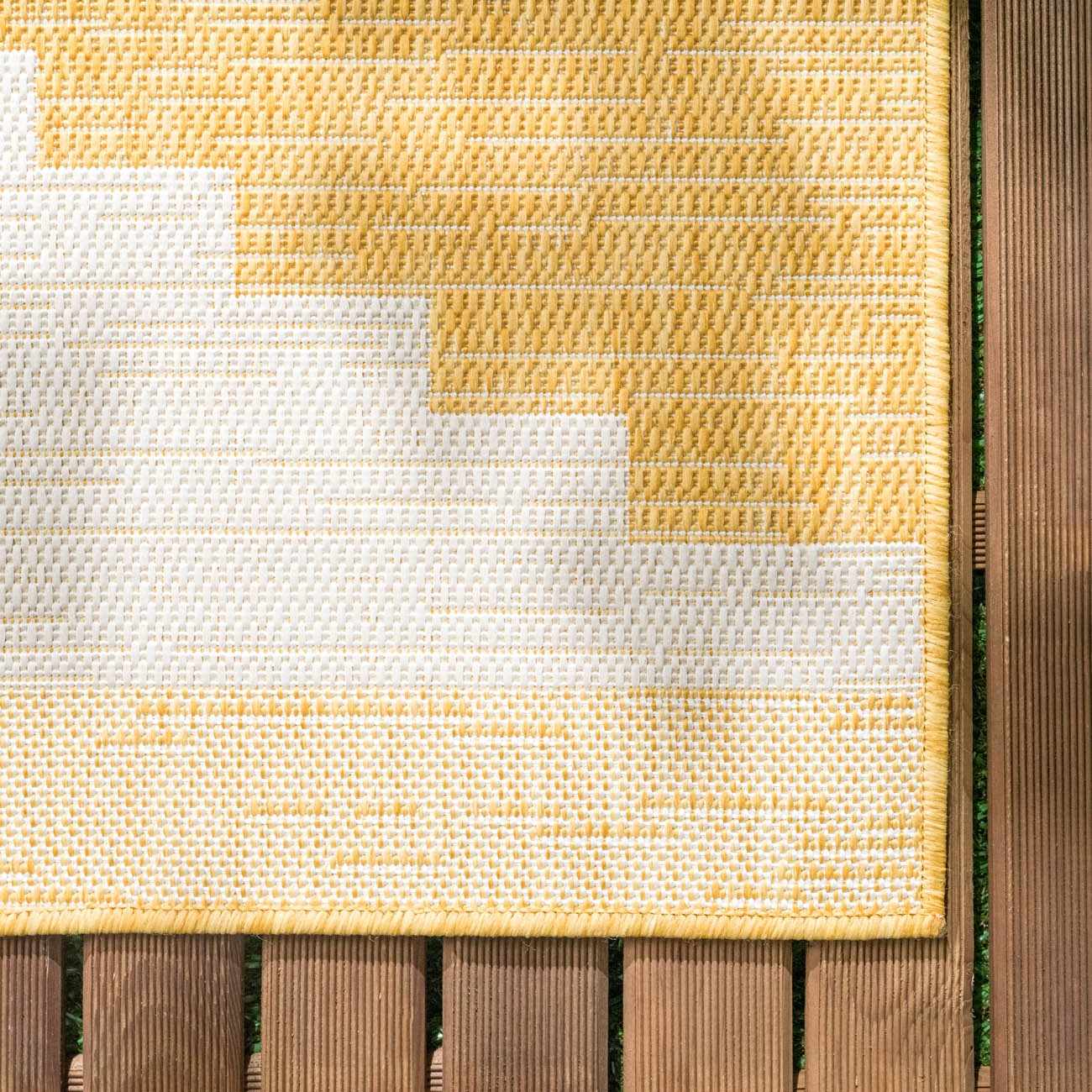 Close-up of the Djugun Yellow Outdoor Rug showing geometric pattern and woven texture on a wood deck. Swatch